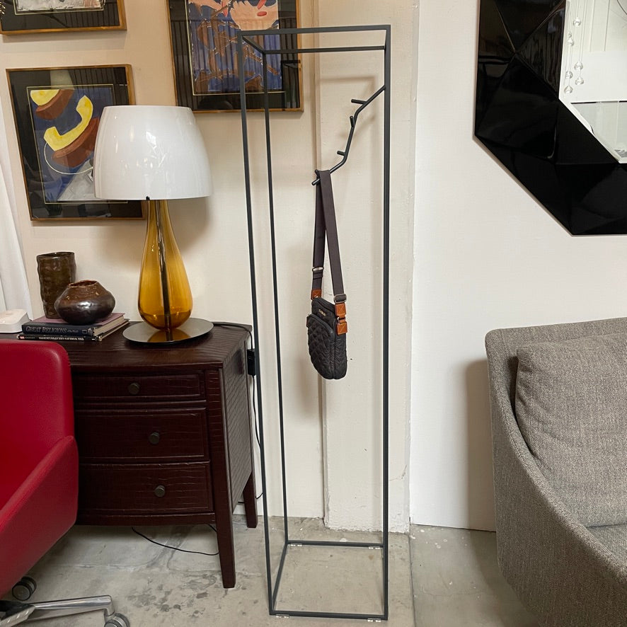 A tall, minimalist, black metal frame structure with an attached hook inside for hanging items, set against a plain white background is the Cappellini Koeda Coat Rack by Cappellini.