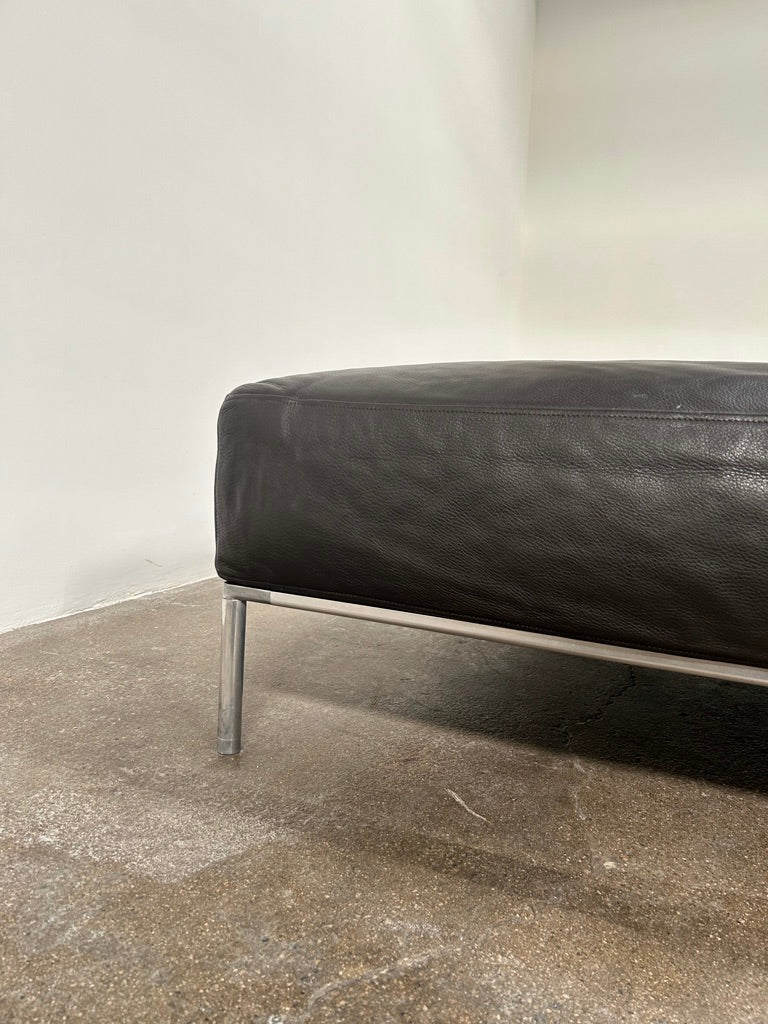 A B&B Italia Frank Ottoman by B&B Italia, featuring a dark brown rectangular cushion and polished aluminum legs, set against a plain background.