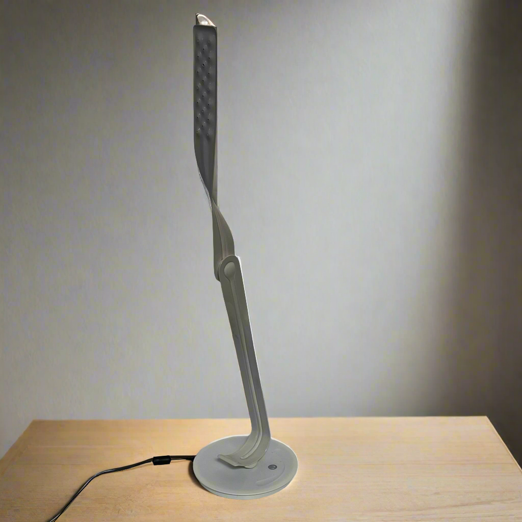 A sleek, modern Herman Miller Leaf Task Light with a curved design on a circular base, connected to a power cord.