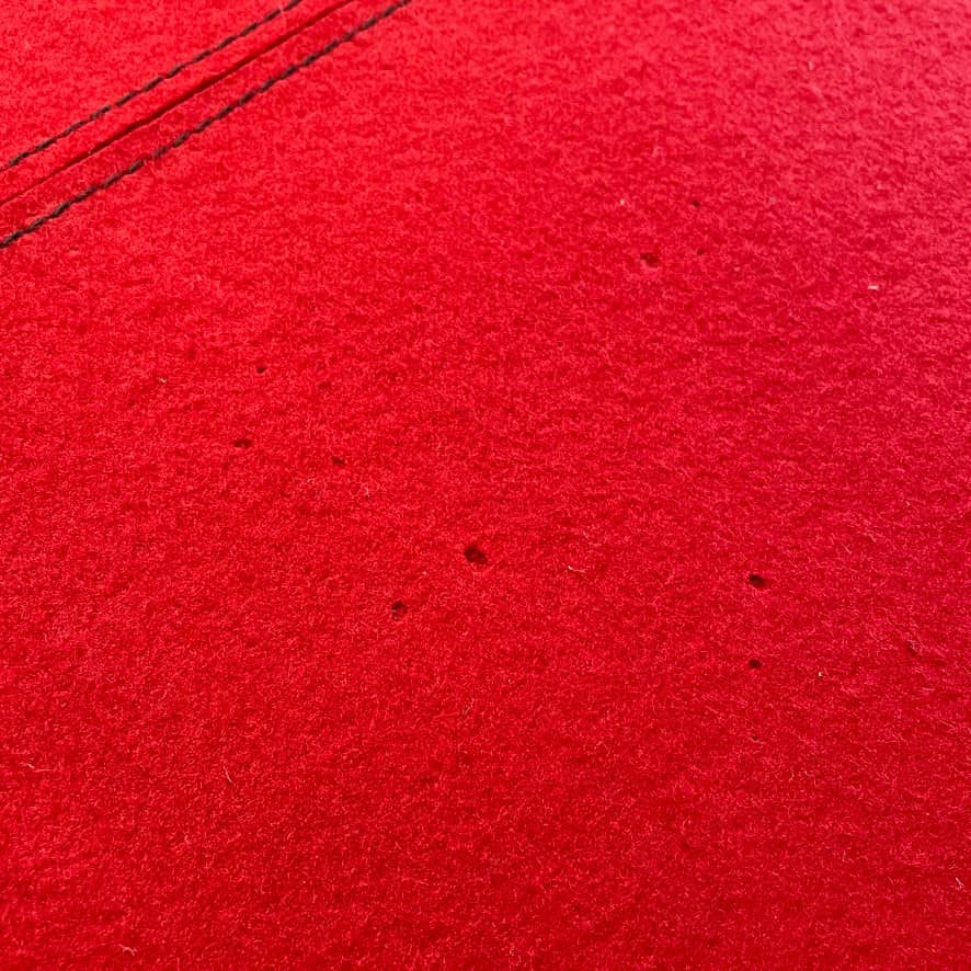 Close-up of the corner of a Large Felt Rug in a vibrant red color against a white background. The fabric showcases a clearly visible seam along its edge.