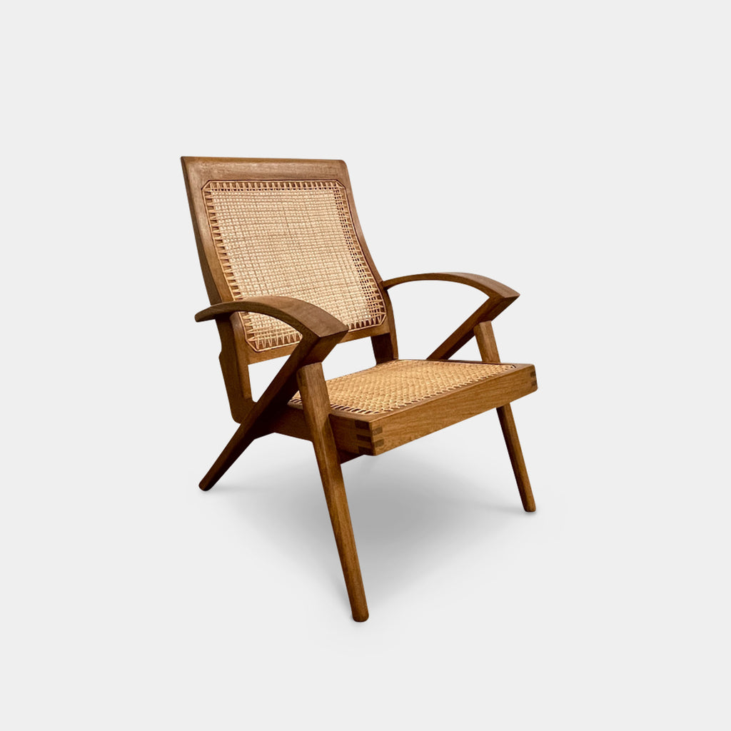 The Claude Home Teak Rex Armchair showcases a sophisticated design with a teak wood frame and a woven rattan seat and backrest, offering a gently reclined silhouette. It stands elegantly on a concrete floor against a plain wall, emanating the timeless charm characteristic of the Claude Home collection.