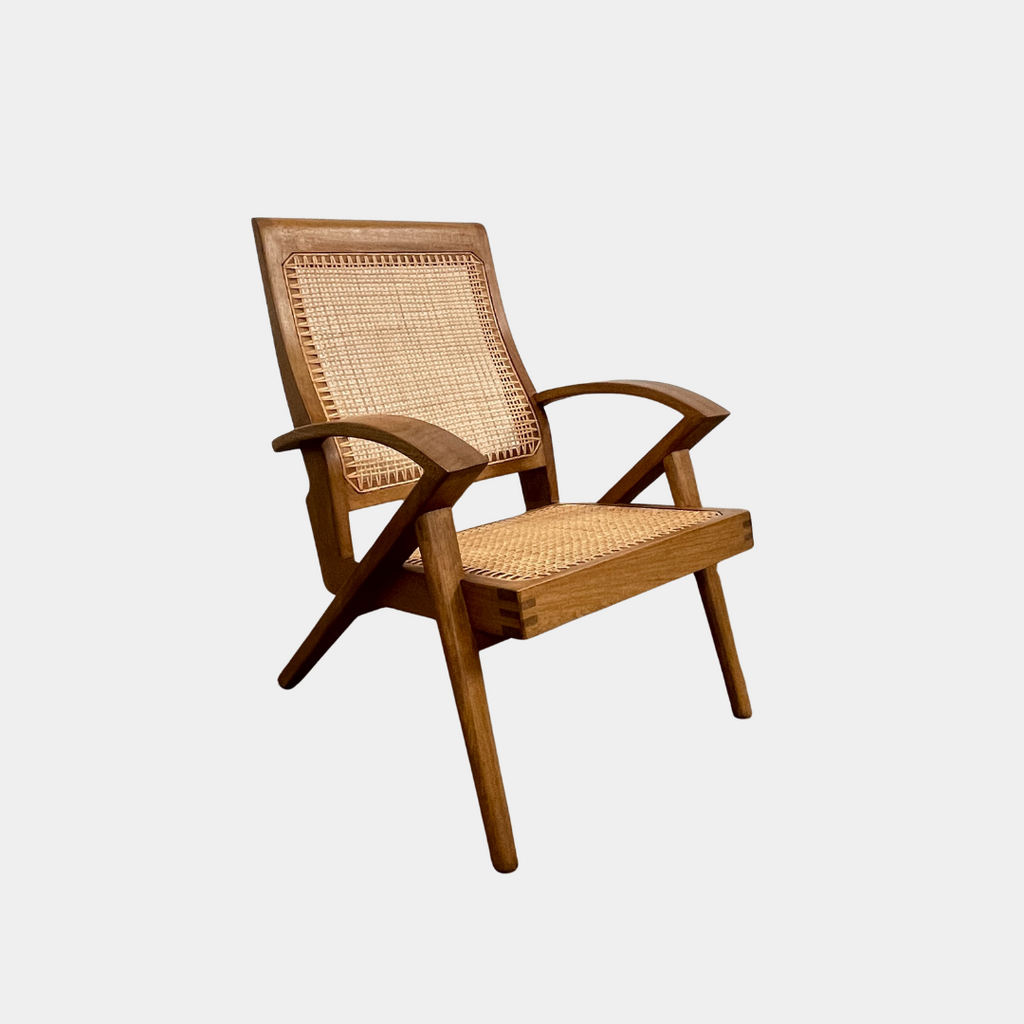 The Claude Home Teak Rex Armchair showcases a sophisticated design with a teak wood frame and a woven rattan seat and backrest, offering a gently reclined silhouette. It stands elegantly on a concrete floor against a plain wall, emanating the timeless charm characteristic of the Claude Home collection.