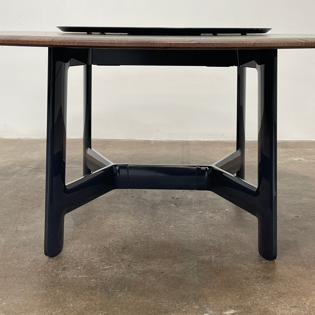 Round wooden table with a central raised circular platform and sleek black legs, reminiscent of the elegant design seen in the B&B Italia Alex Dining Table With Rotating Marble Tray. The rotating marble tray adds a refined touch, making it a versatile centerpiece on a white background.