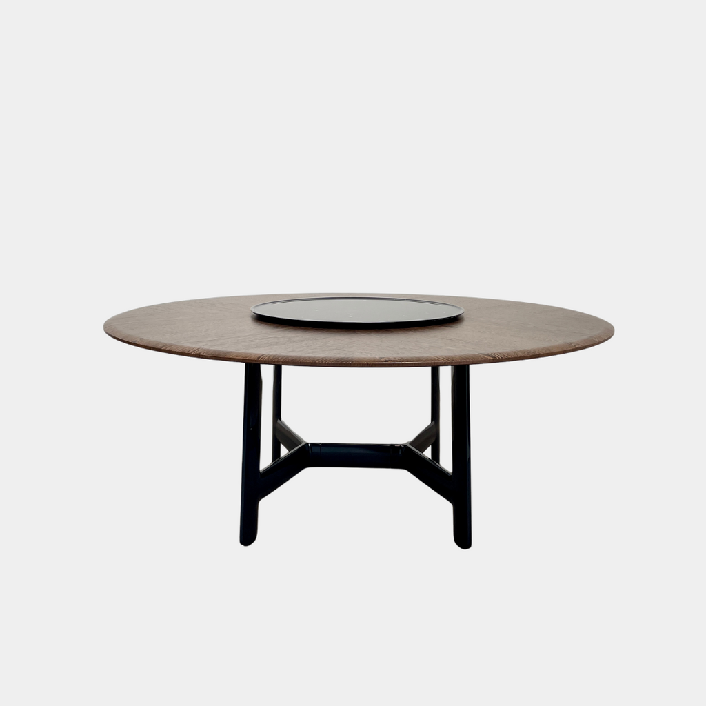 Round wooden table with a central raised circular platform and sleek black legs, reminiscent of the elegant design seen in the B&B Italia Alex Dining Table With Rotating Marble Tray. The rotating marble tray adds a refined touch, making it a versatile centerpiece on a white background.