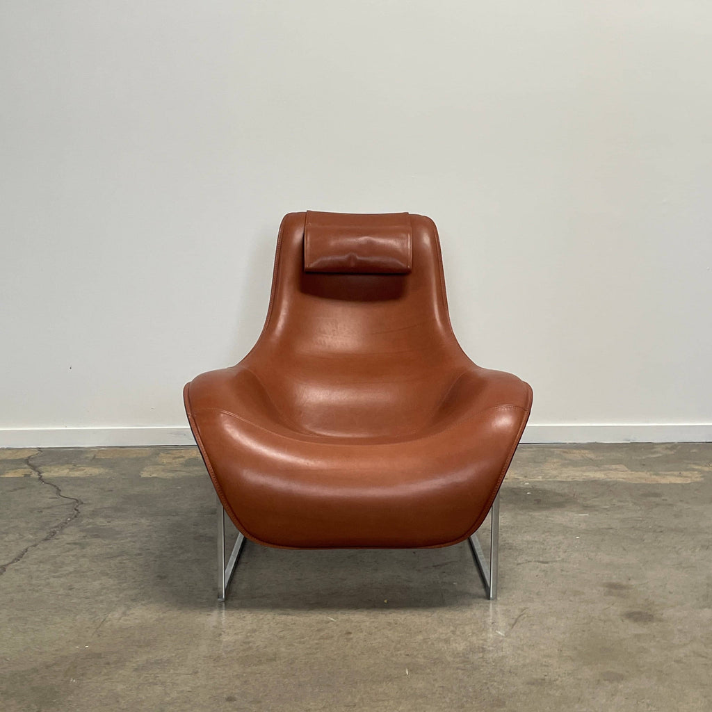 A contemporary brown leather B&B Italia Mart Reclining Armchair, featuring a headrest, is positioned against a minimal gray wall and concrete floor.