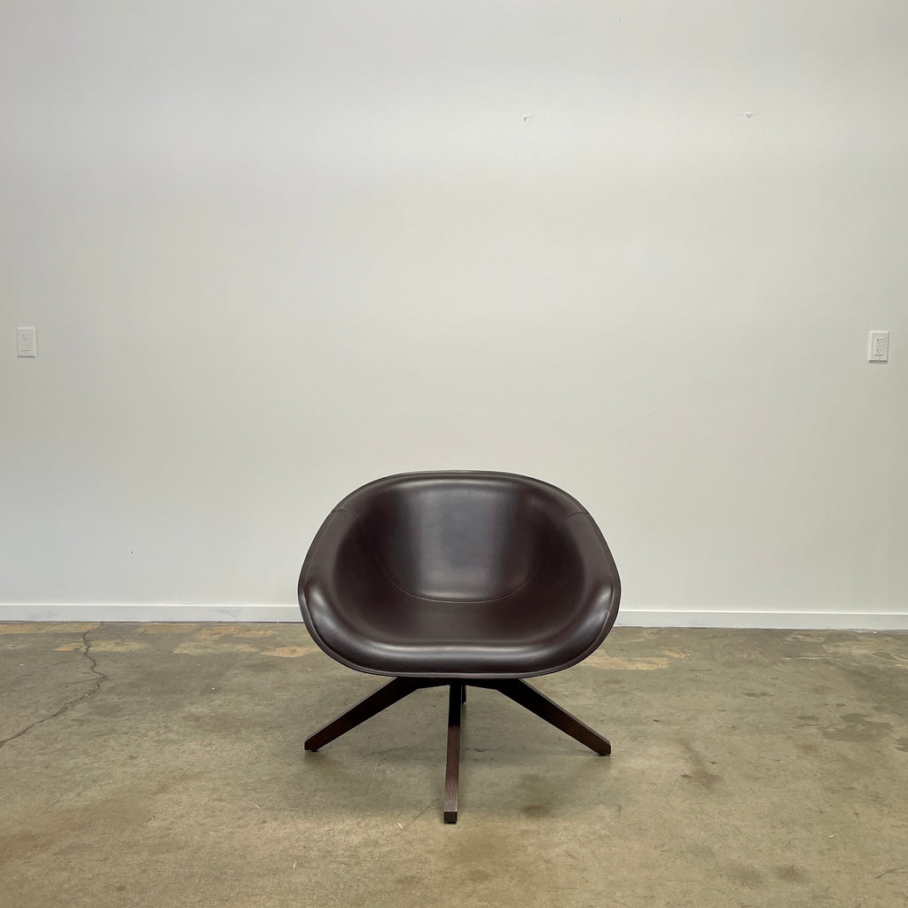 The B&B Italia Mart Swivel Armchair, featuring a rounded seat and four-legged base in a sleek black design, stands elegantly on the concrete floor against a plain white wall.