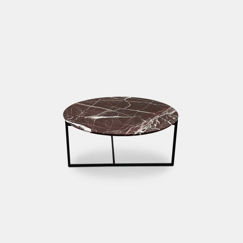 The Baxter Icaro Lepanto Marble Coffee Table showcases a luxurious red and white veined marble top, supported by sleek black metal legs, elegantly positioned on a concrete floor.