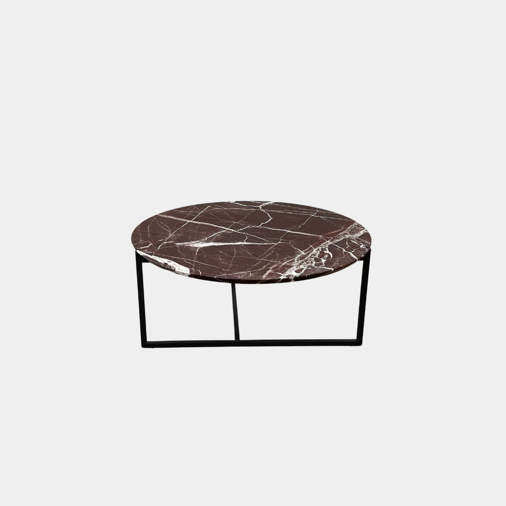 The Baxter Icaro Lepanto Marble Coffee Table showcases a luxurious red and white veined marble top, supported by sleek black metal legs, elegantly positioned on a concrete floor.