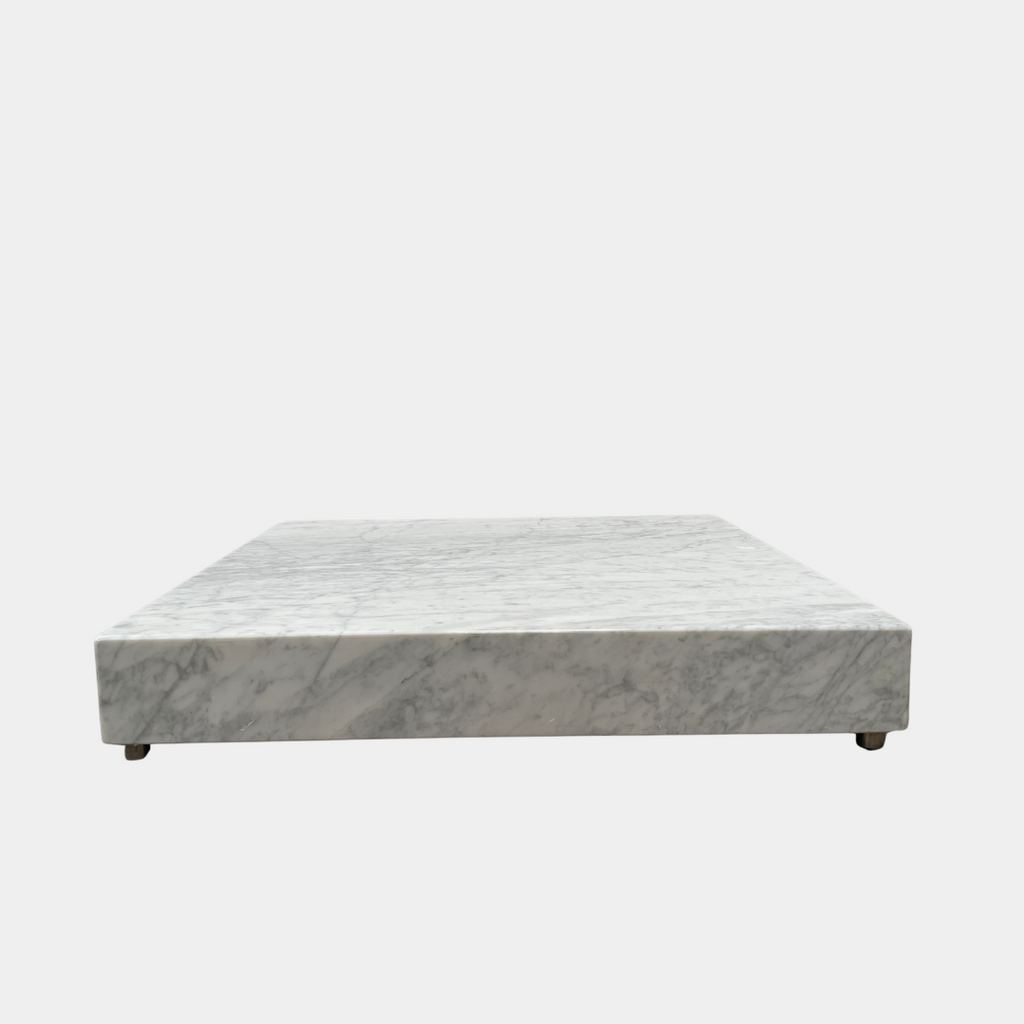 A Carrara Marble Low Coffee Table by Modern Resale with rounded edges sits on a concrete floor in an empty room.