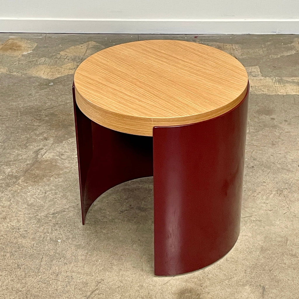 The Cassina Bowy Oak Side Table features a wooden top and a sleek curved burgundy base, set against a white background, echoing Patricia Urquiola's refined design style.