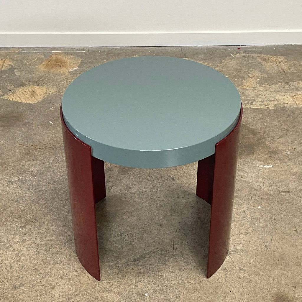 The Cassina Bowy Side Table by Cassina draws from Patricia Urquiola's organic design flair, showcasing a contemporary round structure with a light gray surface and an eye-catching red, curved base.