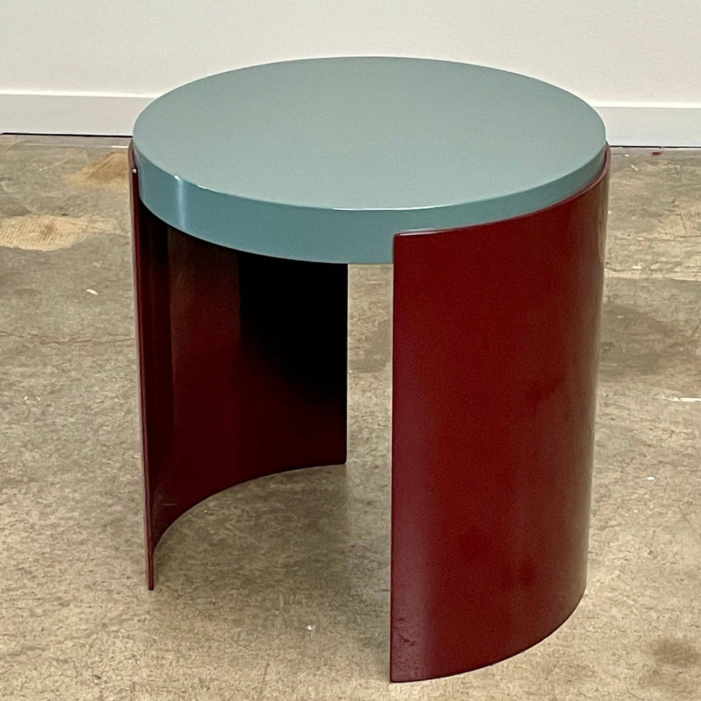 The Cassina Bowy Side Table by Cassina draws from Patricia Urquiola's organic design flair, showcasing a contemporary round structure with a light gray surface and an eye-catching red, curved base.