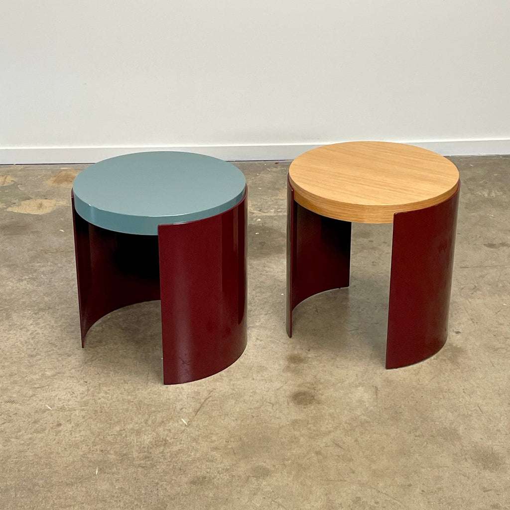 The Cassina Bowy Oak Side Table features a wooden top and a sleek curved burgundy base, set against a white background, echoing Patricia Urquiola's refined design style.