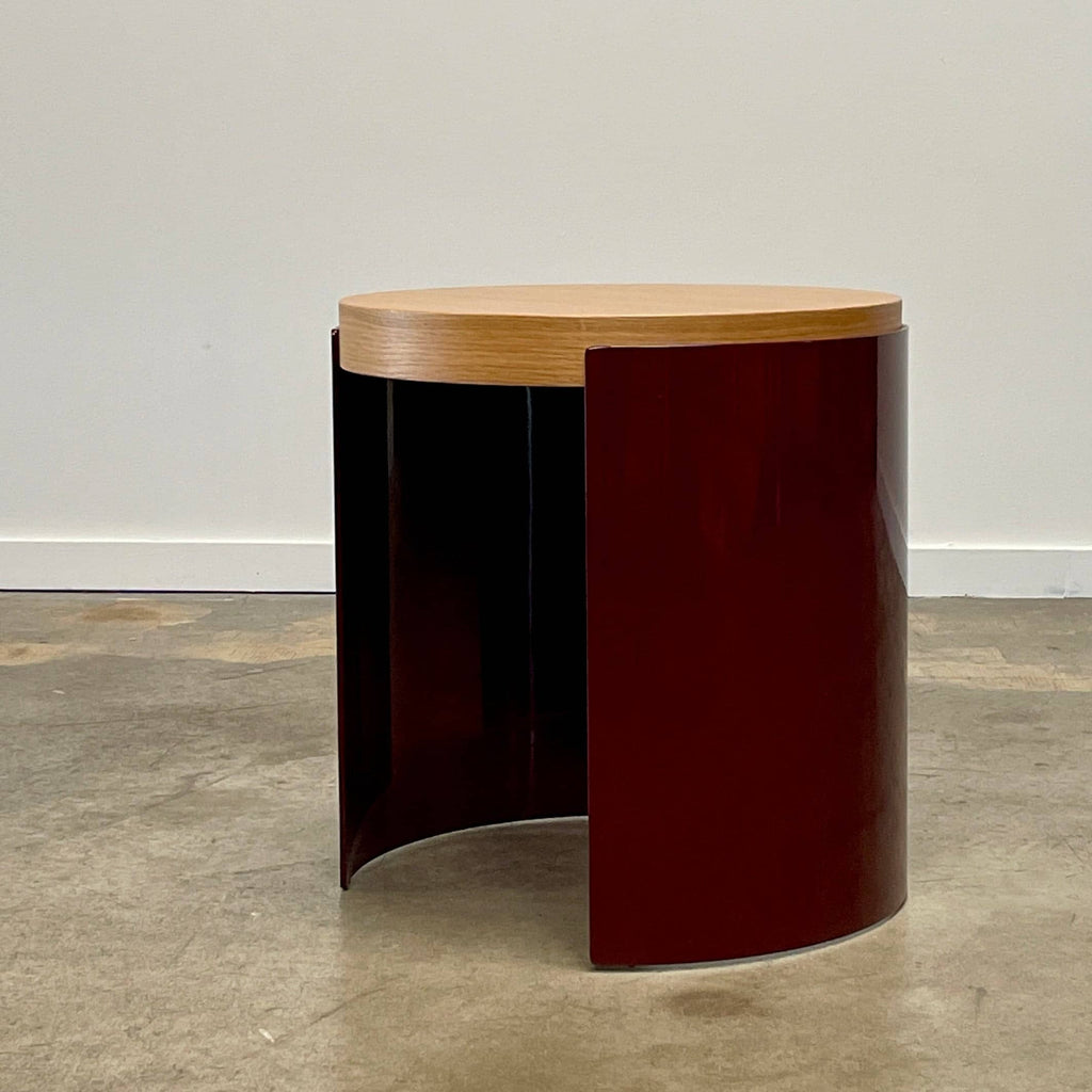 The Cassina Bowy Oak Side Table features a wooden top and a sleek curved burgundy base, set against a white background, echoing Patricia Urquiola's refined design style.