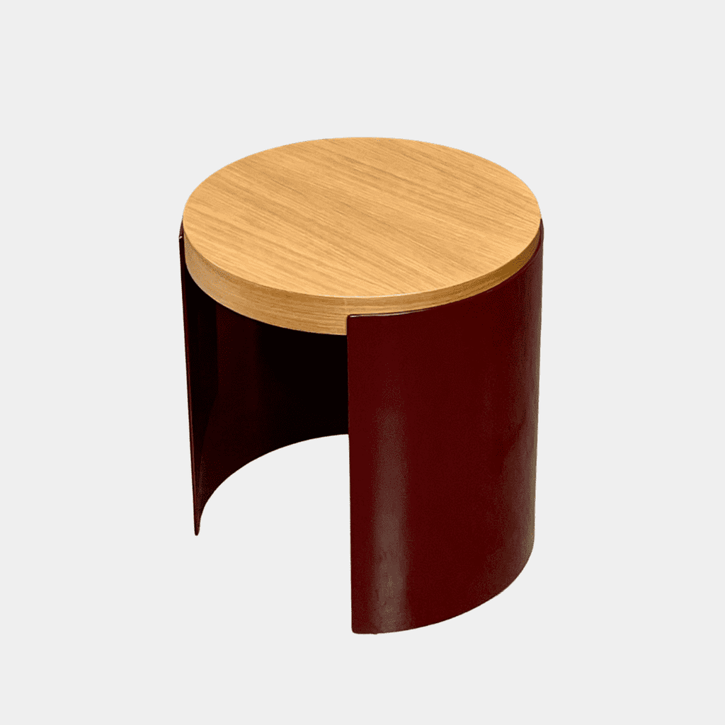 The Cassina Bowy Oak Side Table features a wooden top and a sleek curved burgundy base, set against a white background, echoing Patricia Urquiola's refined design style.