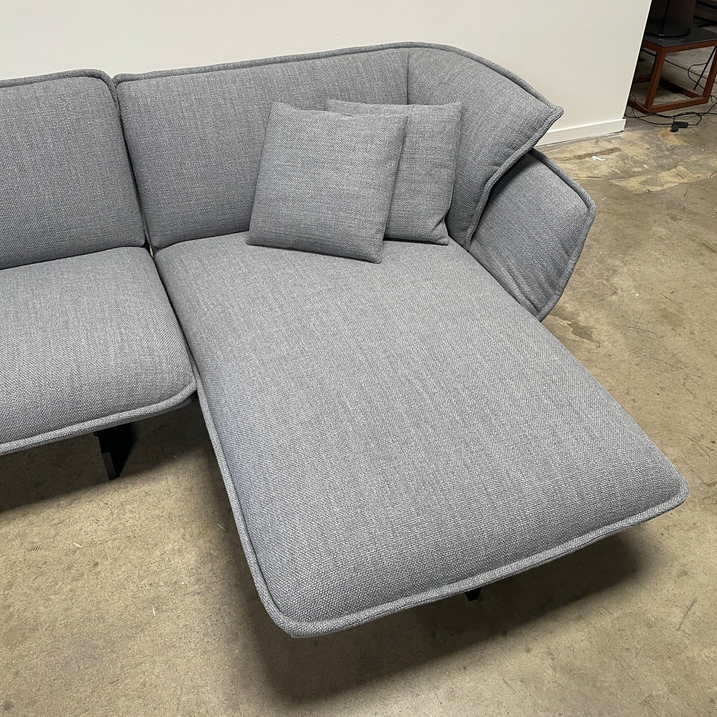 The Cassina Beam Sectional by Cassina, designed by Patricia Urquiola, is a refined gray L-shaped upholstered sectional featuring plush cushions contrasted with a clean white background.