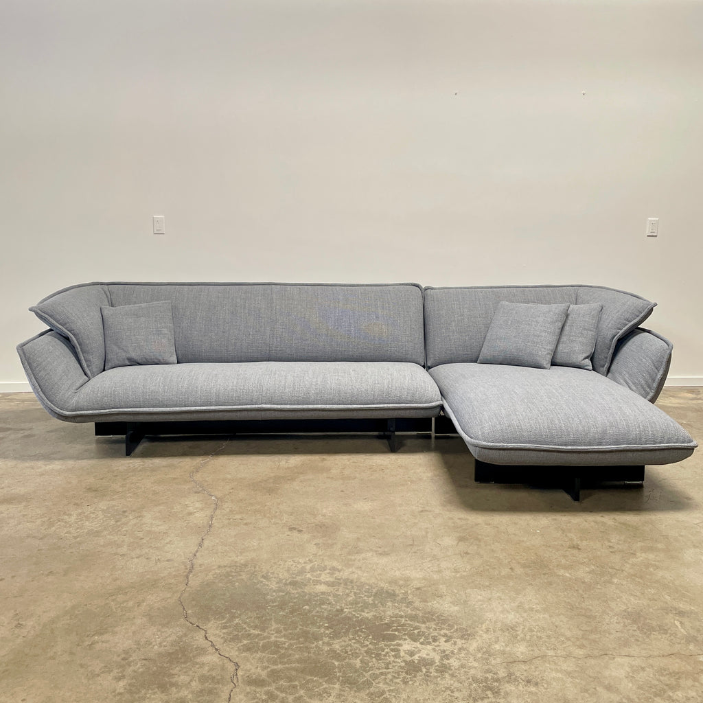 The Cassina Beam Sectional by Cassina, designed by Patricia Urquiola, is a refined gray L-shaped upholstered sectional featuring plush cushions contrasted with a clean white background.