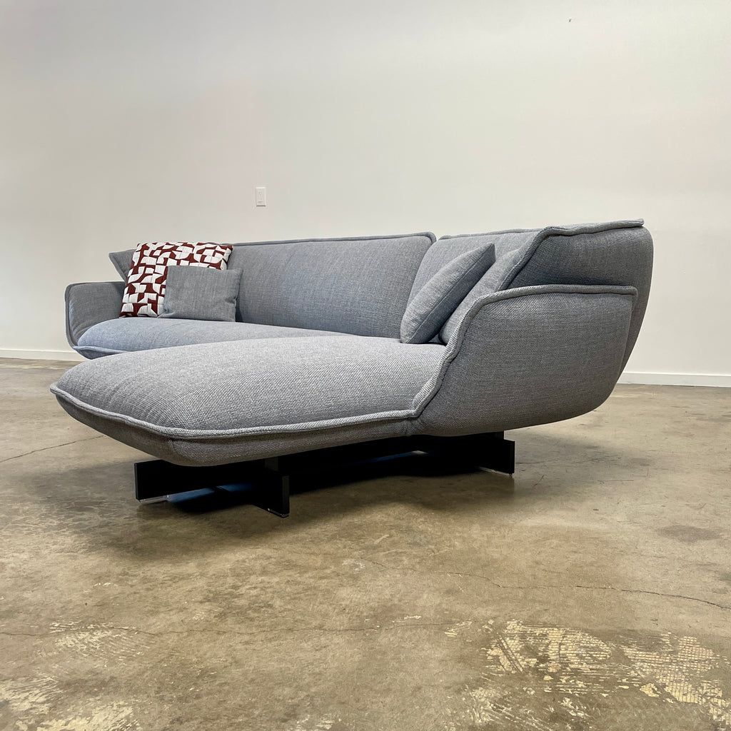 The Cassina Beam Sectional by Cassina, designed by Patricia Urquiola, is a refined gray L-shaped upholstered sectional featuring plush cushions contrasted with a clean white background.