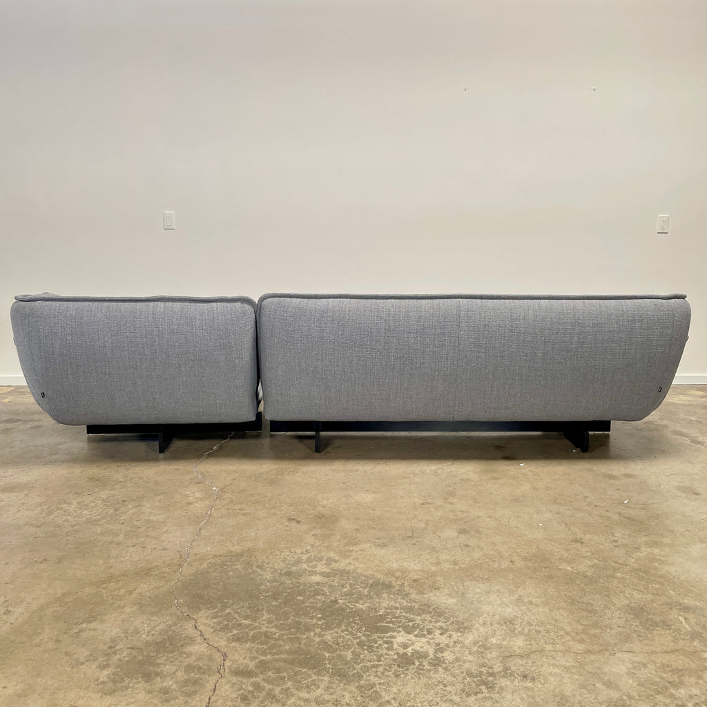 The Cassina Beam Sectional by Cassina, designed by Patricia Urquiola, is a refined gray L-shaped upholstered sectional featuring plush cushions contrasted with a clean white background.