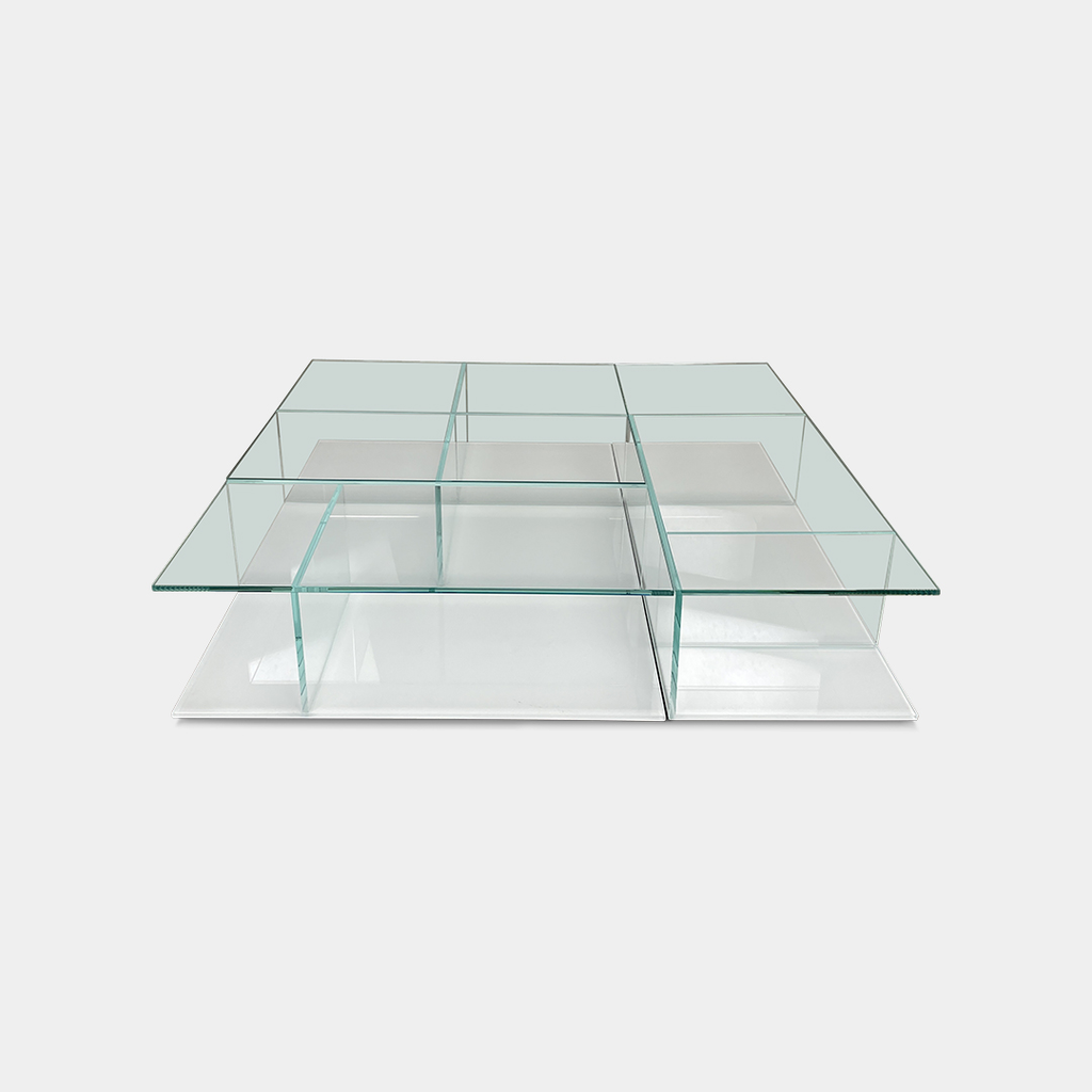 The Cassina Mex Coffee Table, a geometric piece crafted from glass and metal with multiple levels, is reminiscent of a classic Cassina design and sits elegantly on a concrete floor.