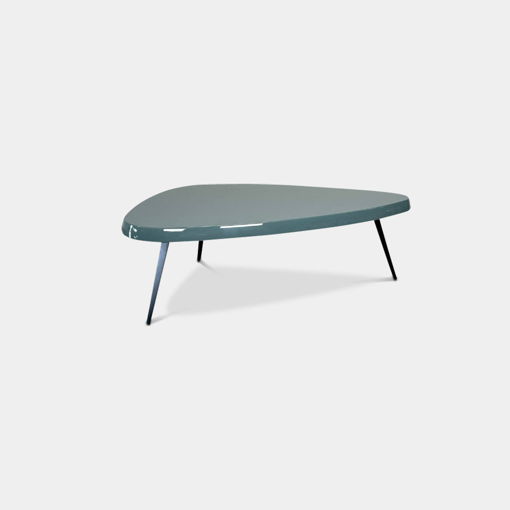 The Cassina Mexique Outdoor Coffee Table is a teal, triangular piece that stands on three slender black legs, creating an elegant contrast against a white background, making it ideal for both indoor and outdoor settings.