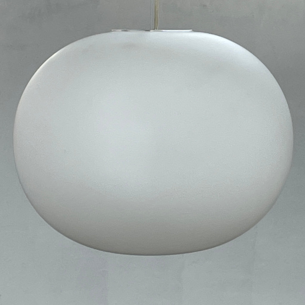 A Flos Glo-Ball S2 Pendant by Flos hangs elegantly from the ceiling, its white, spherical design set against a plain gray background.