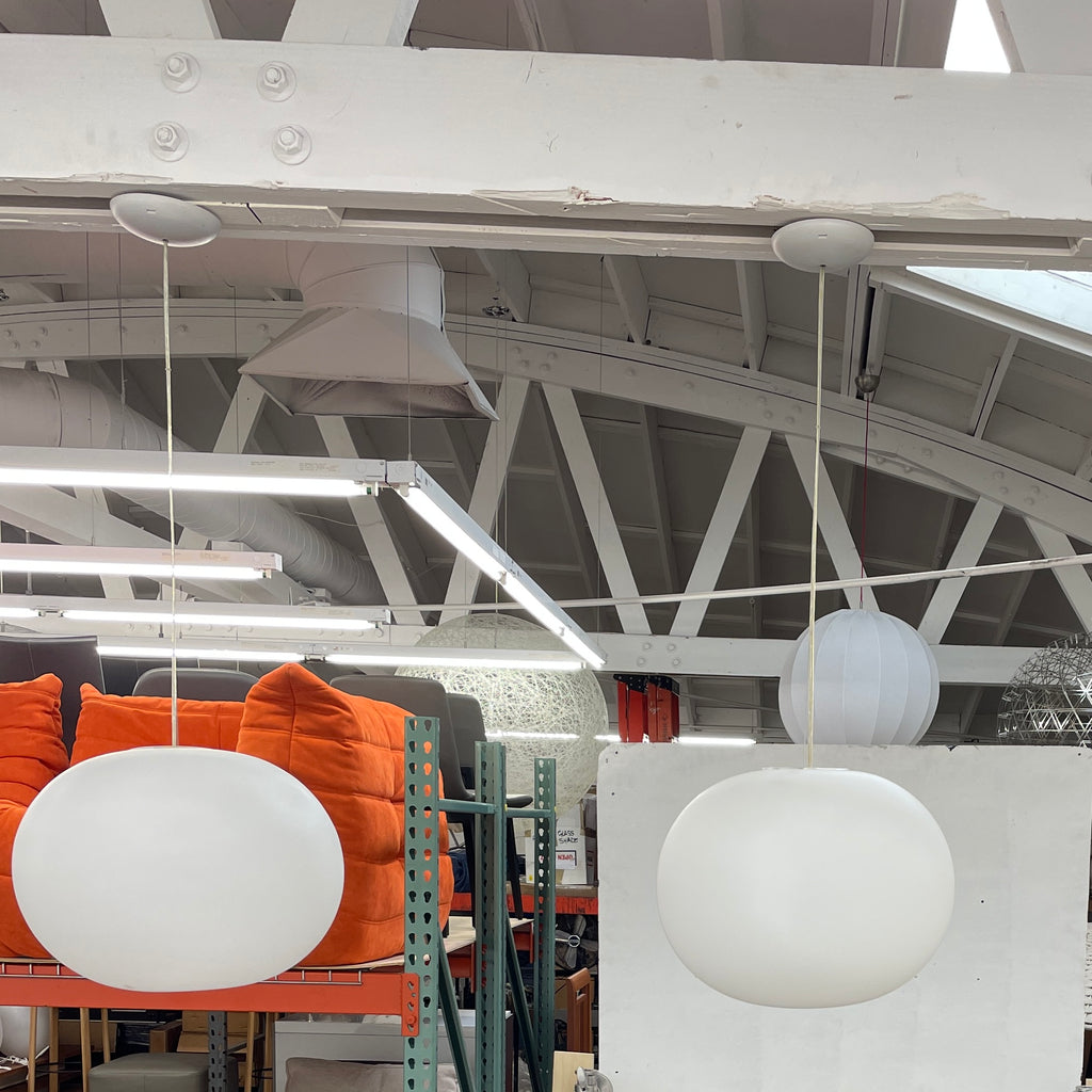 A Flos Glo-Ball S2 Pendant by Flos hangs elegantly from the ceiling, its white, spherical design set against a plain gray background.