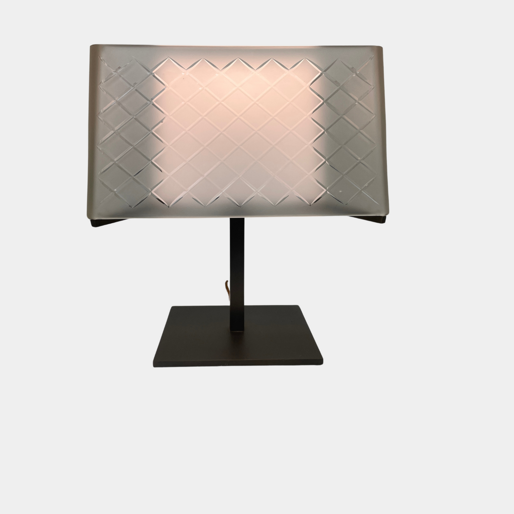 Introducing the Flos Metropolitan Table Light by Flos: a chic table lamp with a rectangular shade adorned with a diamond pattern, gracefully positioned on a square base.