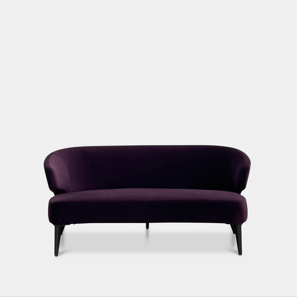 The Minotti Aston Sofa in aubergine velvet, featuring a stylish curved backrest and black legs, is elegantly displayed against a plain white background.