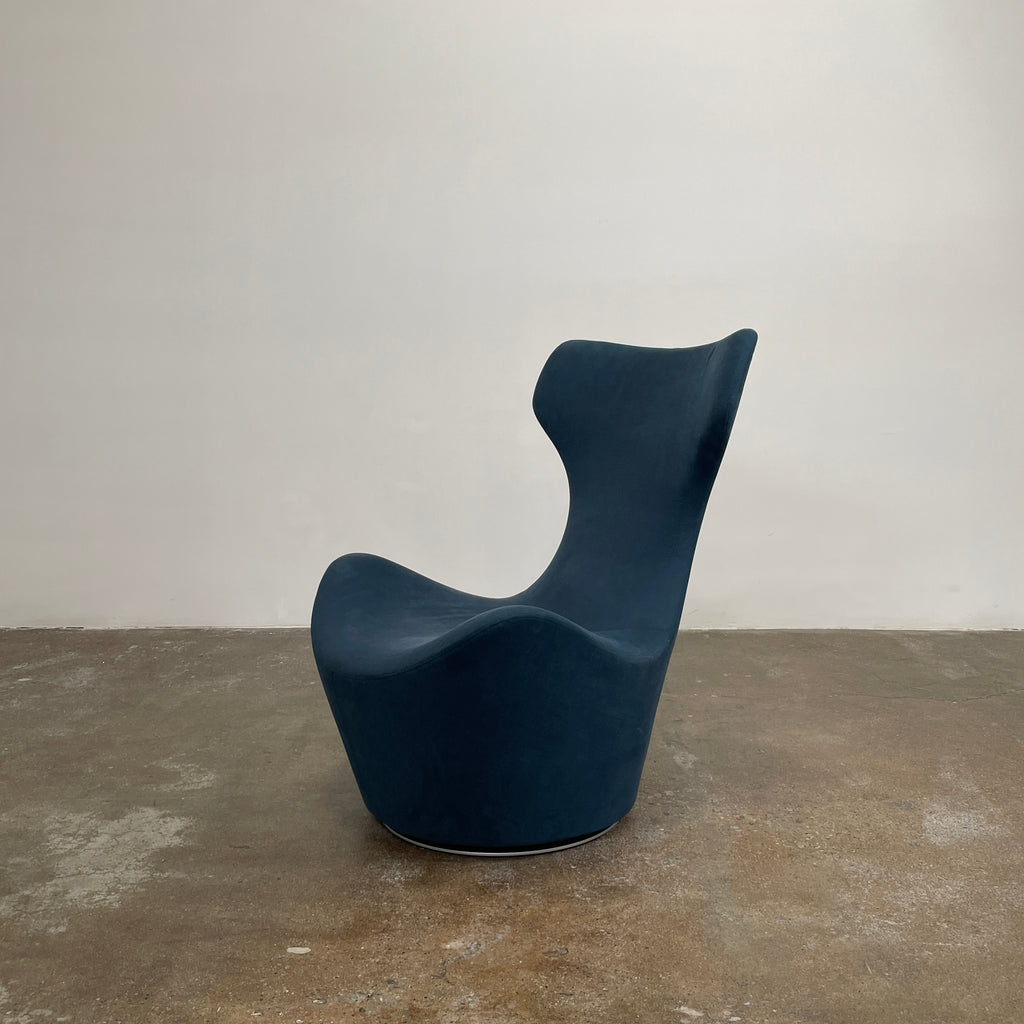 A modern, dark blue B&B Italia Grande Papilio Swivel Chair by Naoto Fukasawa showcases a curved design with a high backrest and wide seat, set against a plain white background.