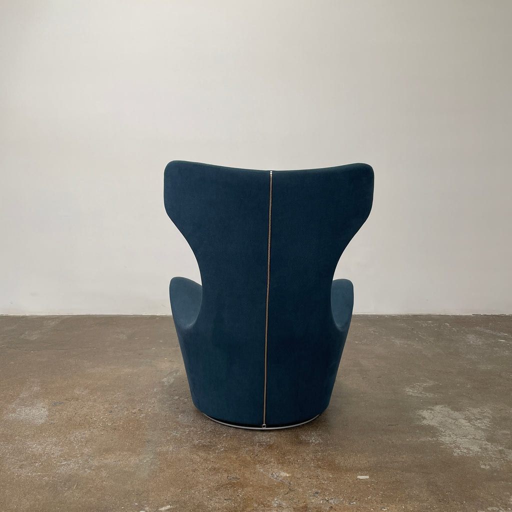 A modern, dark blue B&B Italia Grande Papilio Swivel Chair by Naoto Fukasawa showcases a curved design with a high backrest and wide seat, set against a plain white background.