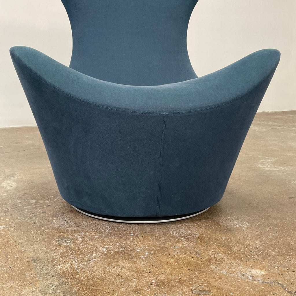 A modern, dark blue B&B Italia Grande Papilio Swivel Chair by Naoto Fukasawa showcases a curved design with a high backrest and wide seat, set against a plain white background.