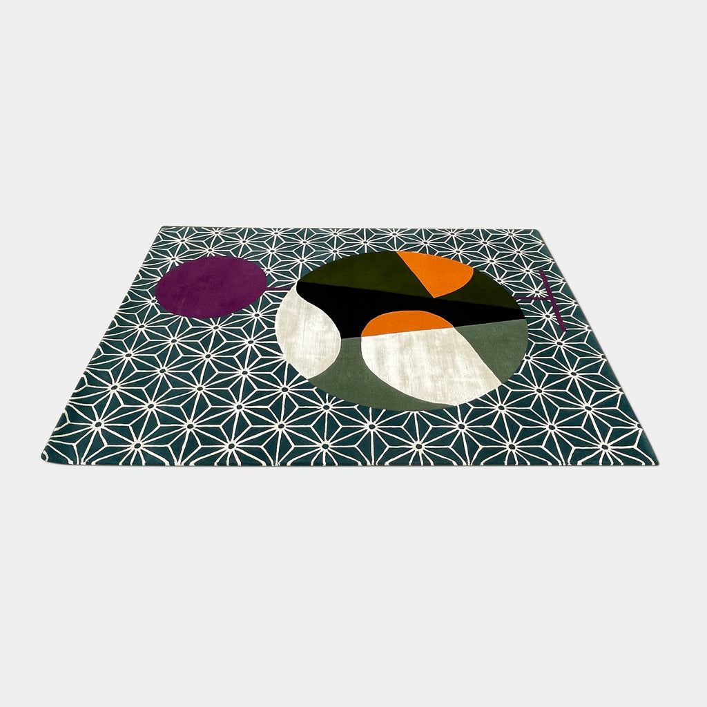 The Maison Dada Japanese Abstraction No5 Rug showcases a geometric pattern with a striking central circle in orange, green, and cream. A smaller purple circle enhances the design, complemented by a white star pattern on a green background reminiscent of Japanese abstraction.