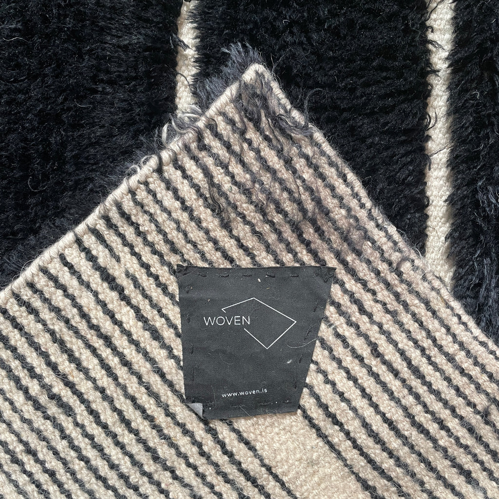 Close-up of a Woven Dilla Black & Ivory wool rug with diagonal white stitching, creating a distinct pattern on a high/low pile surface.