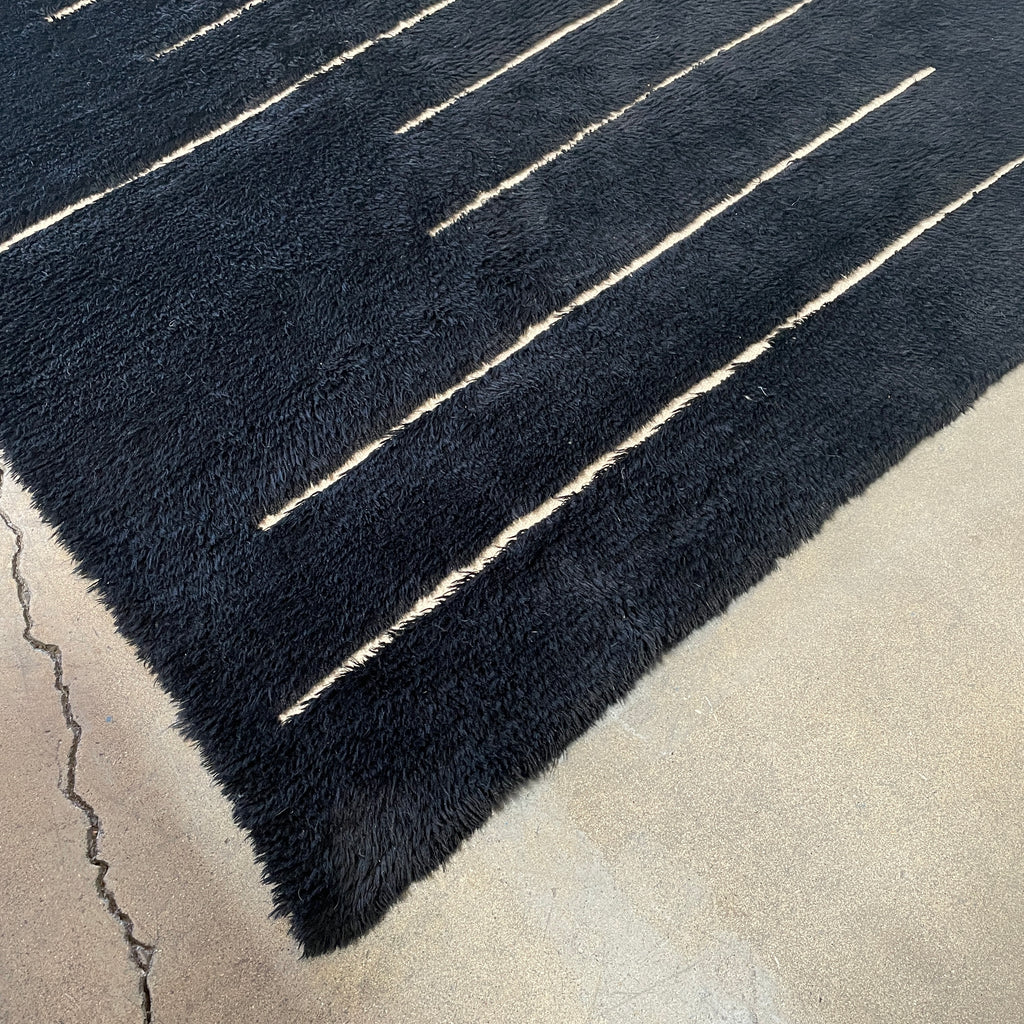 Close-up of a Woven Dilla Black & Ivory wool rug with diagonal white stitching, creating a distinct pattern on a high/low pile surface.