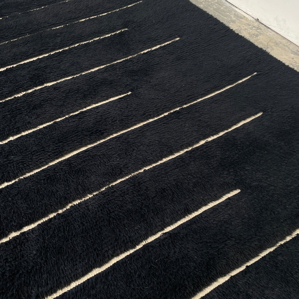 Close-up of a Woven Dilla Black & Ivory wool rug with diagonal white stitching, creating a distinct pattern on a high/low pile surface.