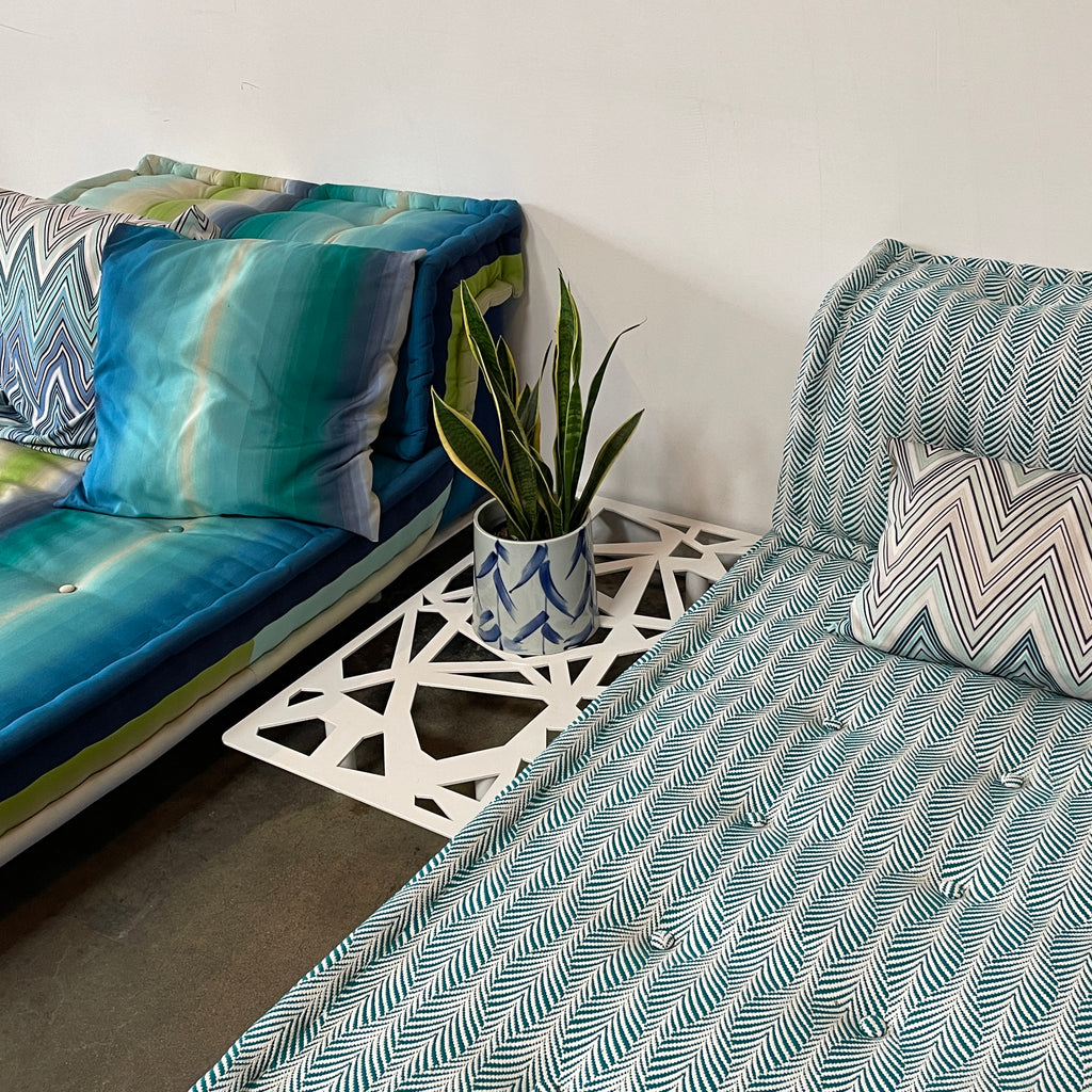 A modern, multicolored Roche Bobois Mah Jong Chaise Lounge from Roche Bobois with a gradient pattern in blue, green, and yellow shades, featuring a cushioned backrest and a matching pillow on a white base for perfect outdoor relaxation.