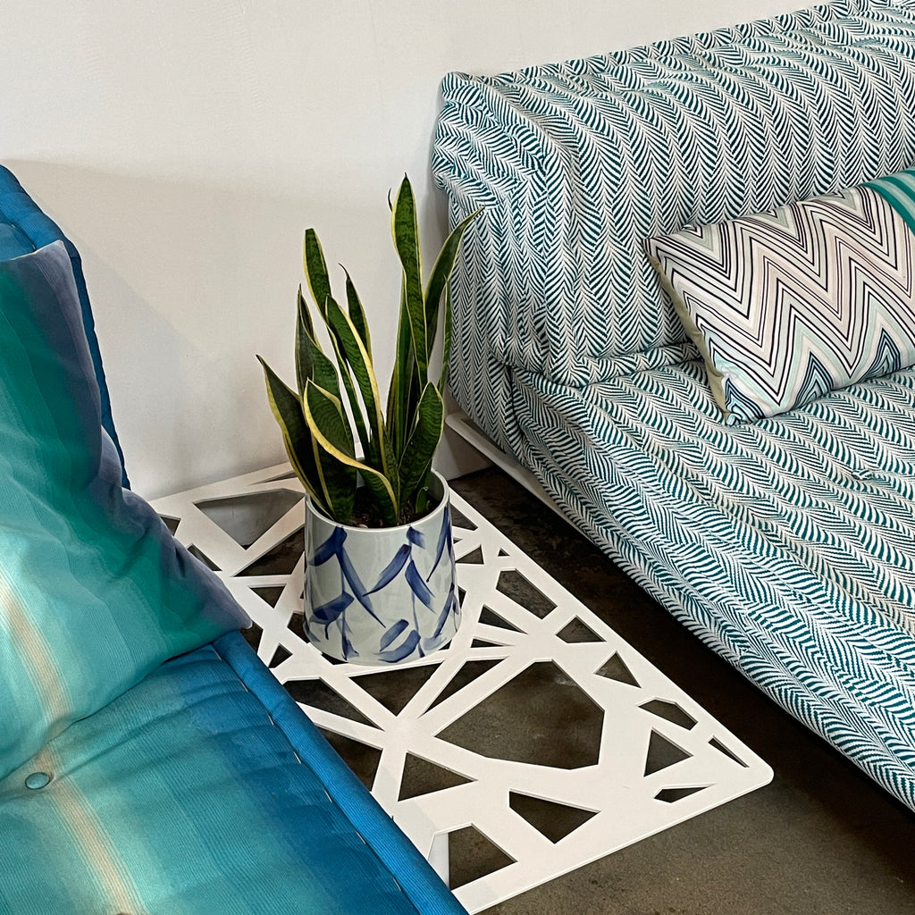 A colorful cushioned bench with stacked pillows next to a Roche Bobois Mah Jong Outdoor Side Table on a wooden floor.