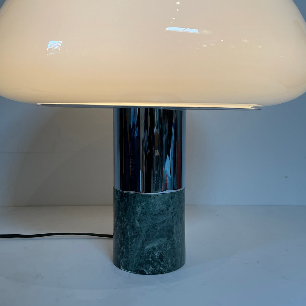 The Nahoor K&W Table Light features a large, dome-shaped beige shade and a cylindrical base crafted with exquisite Murano glass. This elegant piece reflects Italian design and sophistication, complete with a black power cord and switch.