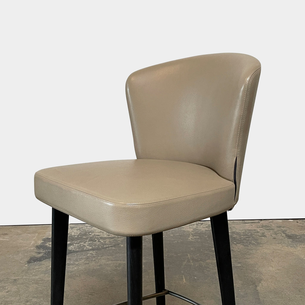 A pair of Minotti Aston Counter Stools, featuring beige cushioned backs and seats supported by sleek black-finished solid ash legs, is displayed against a plain background.