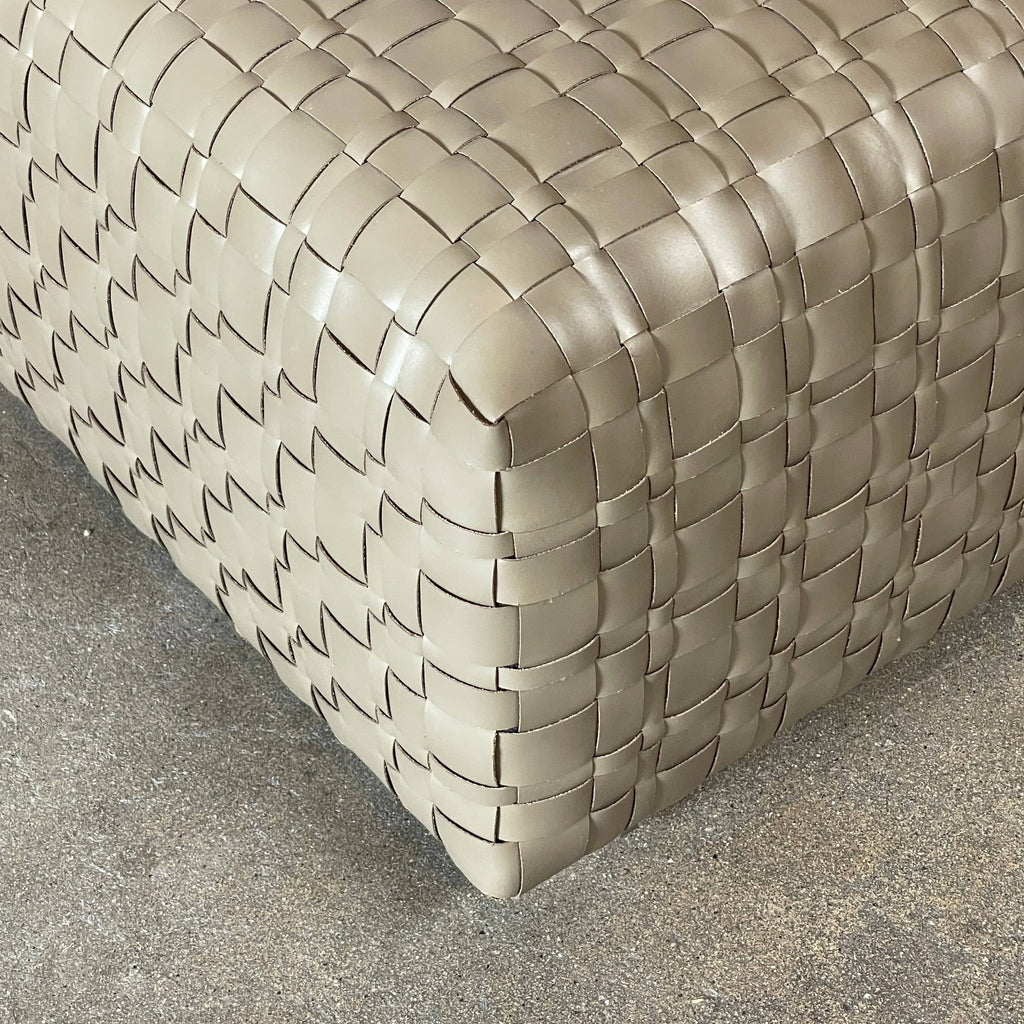 A square, beige Flexform Bangkok Ottoman with a woven leather pattern and four short metal legs evokes the stylish charm of Bangkok.