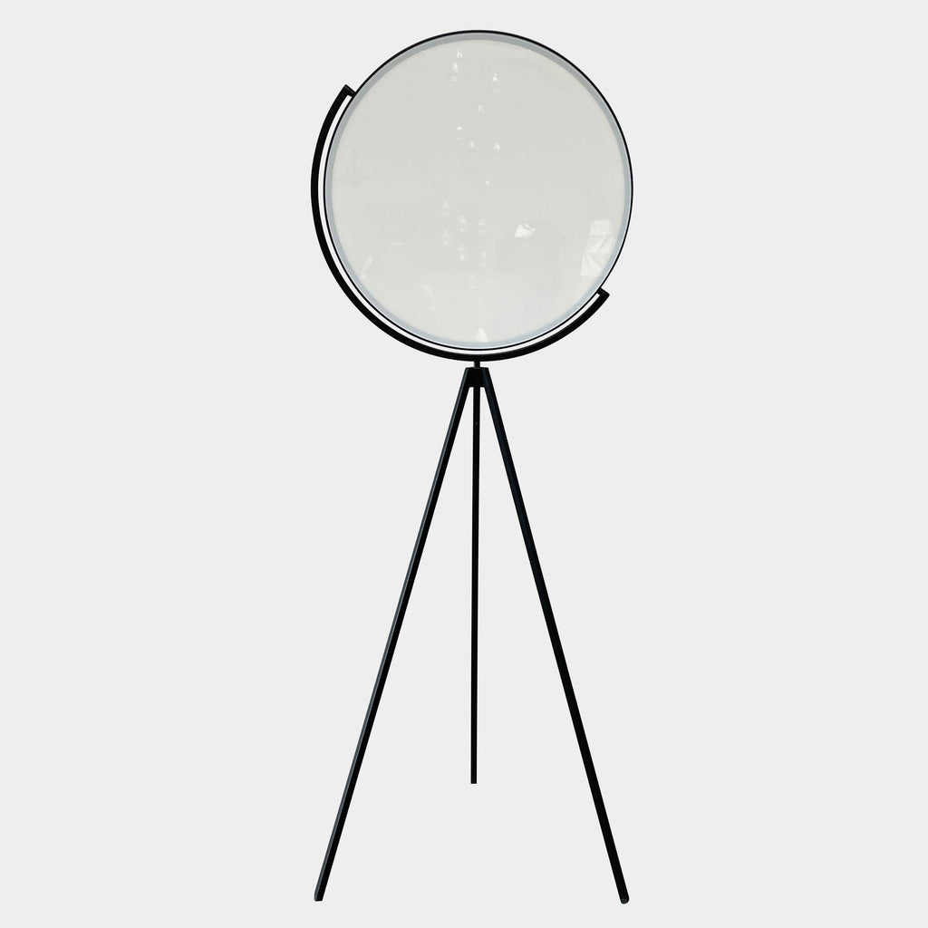 A large circular mirror set in a black metal frame on a tripod stand, isolated against a white background, exudes sophistication akin to the Flos Superloon Floor Light by Flos, providing broad and diffused light that can be dimmed for any ambiance.