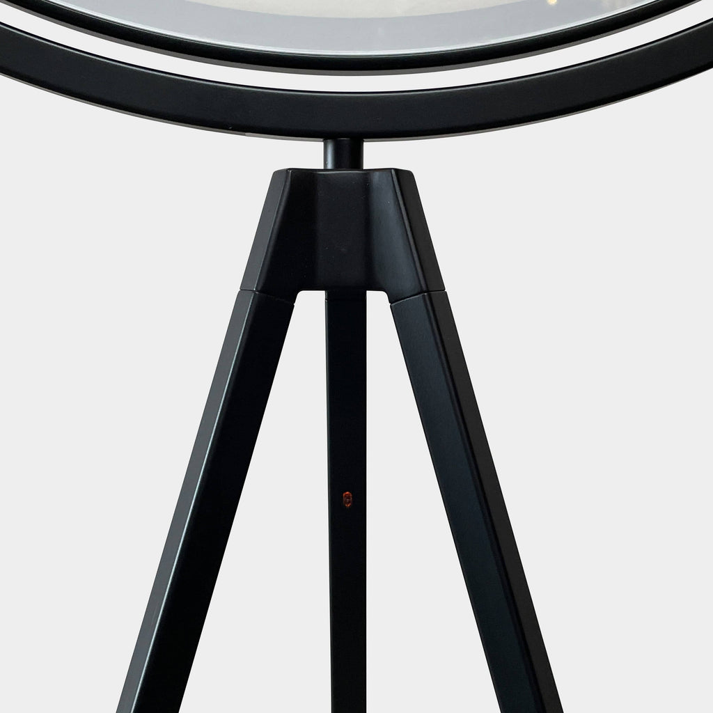 A large circular mirror set in a black metal frame on a tripod stand, isolated against a white background, exudes sophistication akin to the Flos Superloon Floor Light by Flos, providing broad and diffused light that can be dimmed for any ambiance.