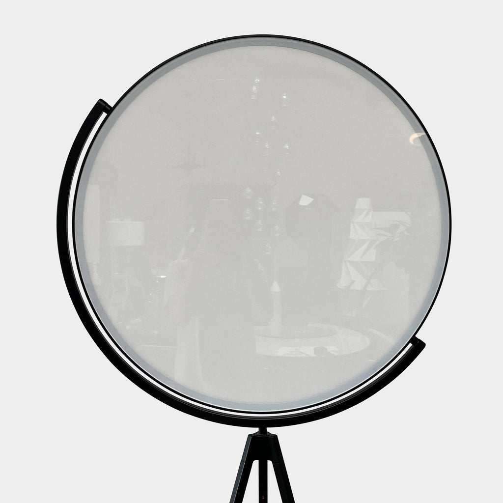 A large circular mirror set in a black metal frame on a tripod stand, isolated against a white background, exudes sophistication akin to the Flos Superloon Floor Light by Flos, providing broad and diffused light that can be dimmed for any ambiance.