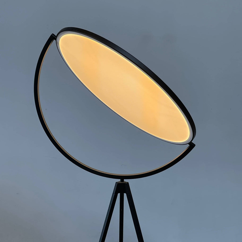 A large circular mirror set in a black metal frame on a tripod stand, isolated against a white background, exudes sophistication akin to the Flos Superloon Floor Light by Flos, providing broad and diffused light that can be dimmed for any ambiance.