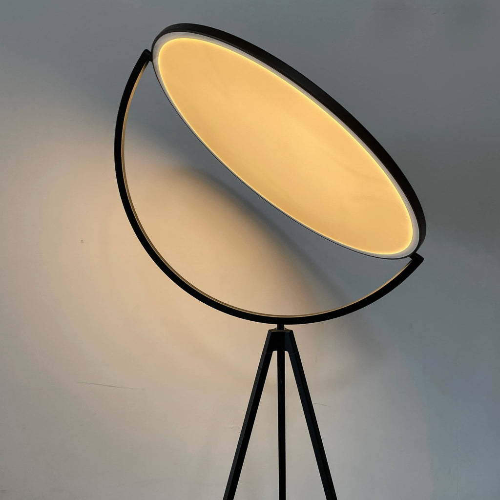 A large circular mirror set in a black metal frame on a tripod stand, isolated against a white background, exudes sophistication akin to the Flos Superloon Floor Light by Flos, providing broad and diffused light that can be dimmed for any ambiance.