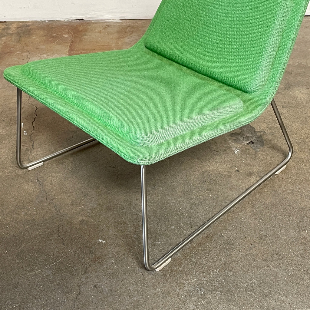 A Cappellini Low Pad Lounge Chair with a metal frame, reminiscent of Jasper Morrison's design, sits next to a small, round side table holding a cup and saucer, a notebook, and a pen. The setting is a minimalist indoor space with a concrete floor.