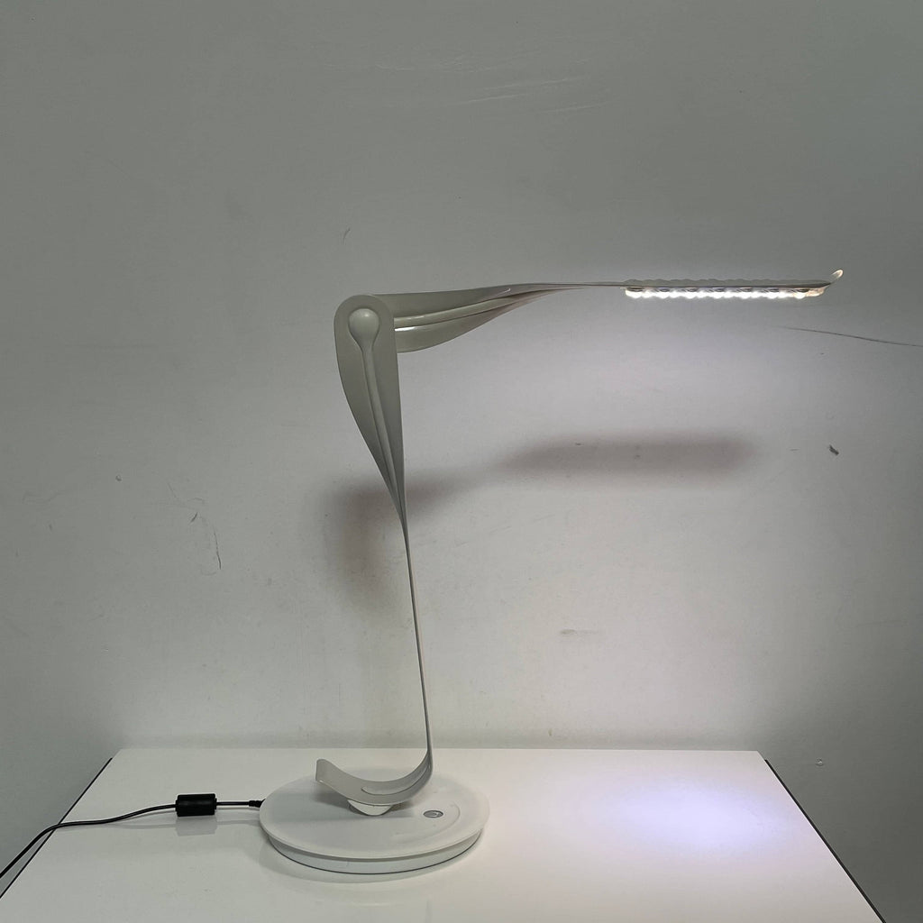 A sleek, modern Herman Miller Leaf Task Light with a curved design on a circular base, connected to a power cord.