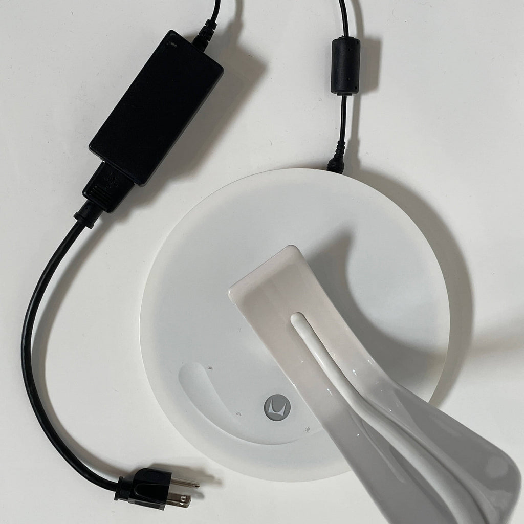 A sleek, modern Herman Miller Leaf Task Light with a curved design on a circular base, connected to a power cord.