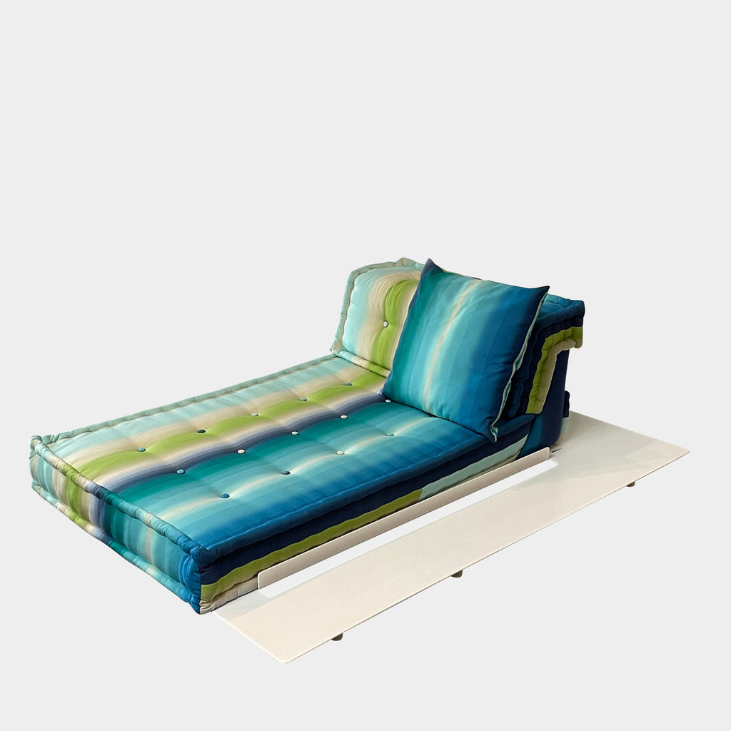 A modern, multicolored Roche Bobois Mah Jong Chaise Lounge from Roche Bobois with a gradient pattern in blue, green, and yellow shades, featuring a cushioned backrest and a matching pillow on a white base for perfect outdoor relaxation.